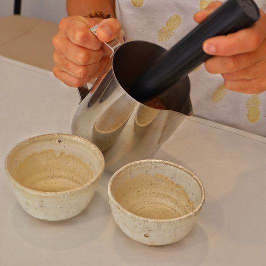 Manos de persona preparnado cacao con 2 tazas vacías para llenar