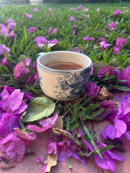 Taza de cacao femenino rodeado de flores moradas y sobre césped