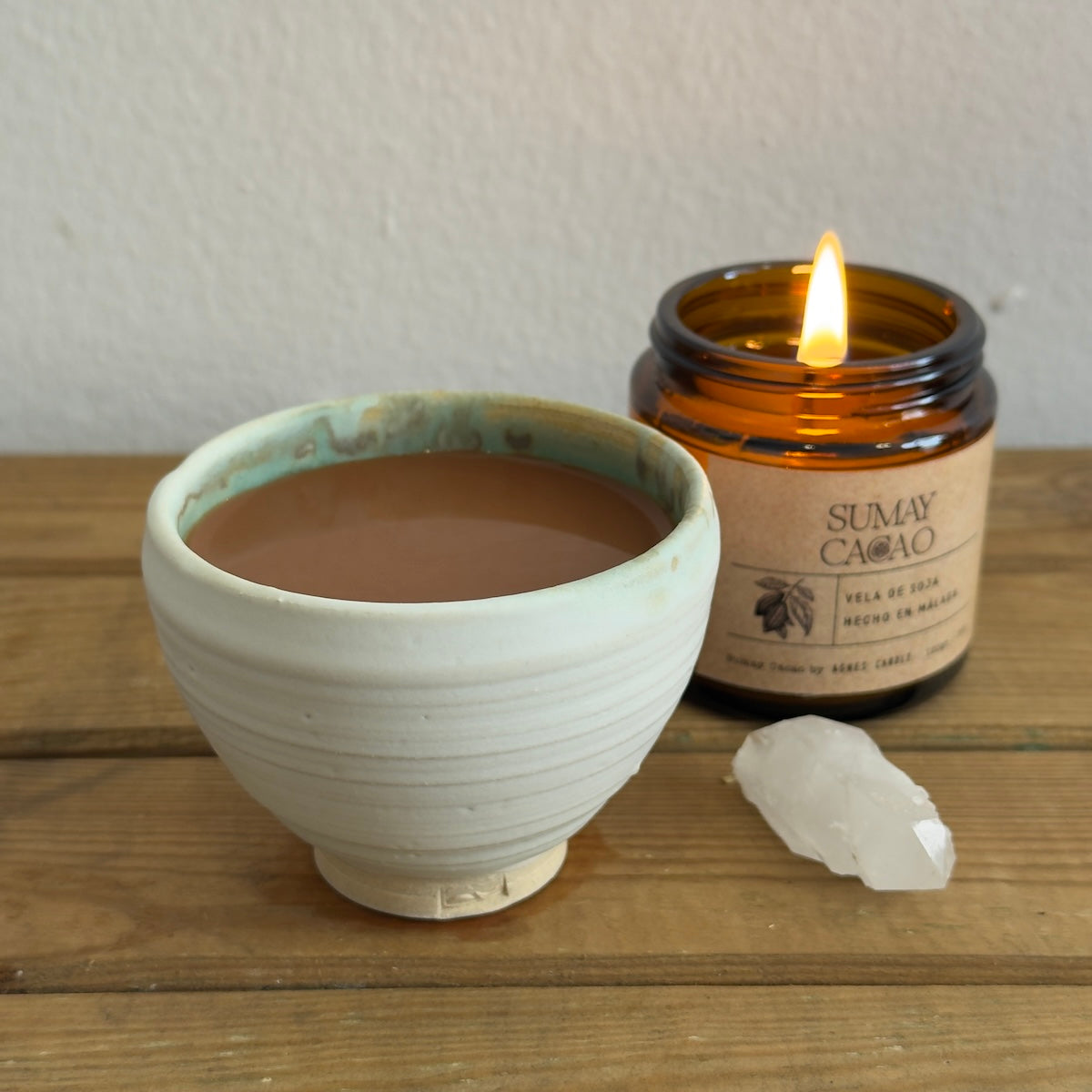 Taza artesanal con cacao ceremonial acompañada de vela y cuarzo con fondo blanco.