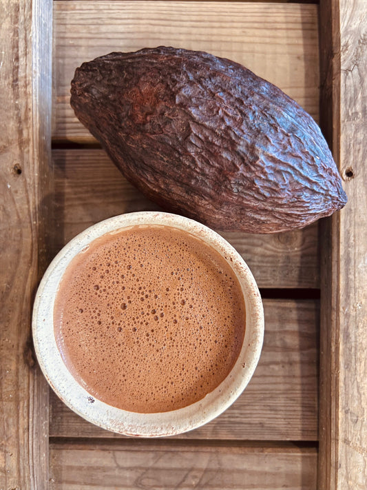 Taza de cacao ceremonial y fruto sobre madera