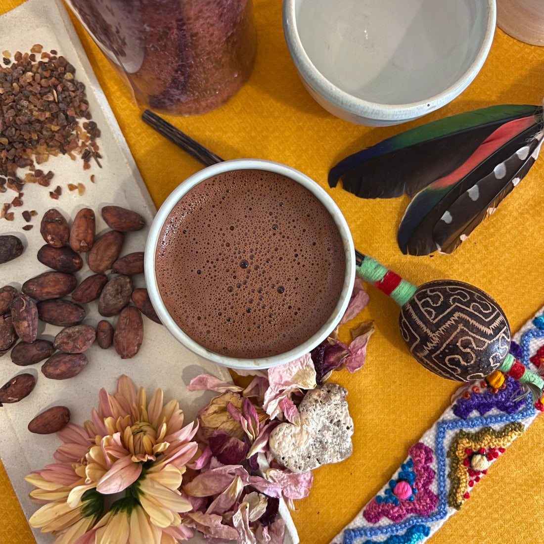 Cacao ceremonial preparado junto a semillas, nibs y objetos rituales sobre un mantel cálido.