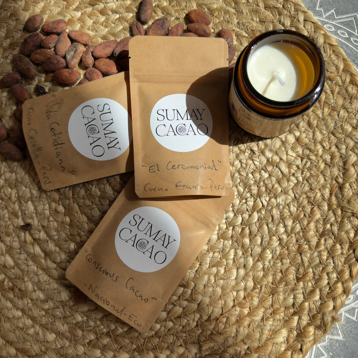 Paquetes de 25g de cacao ceremonial con semillas de cacao y vela sobre fondo marrón claro y gris