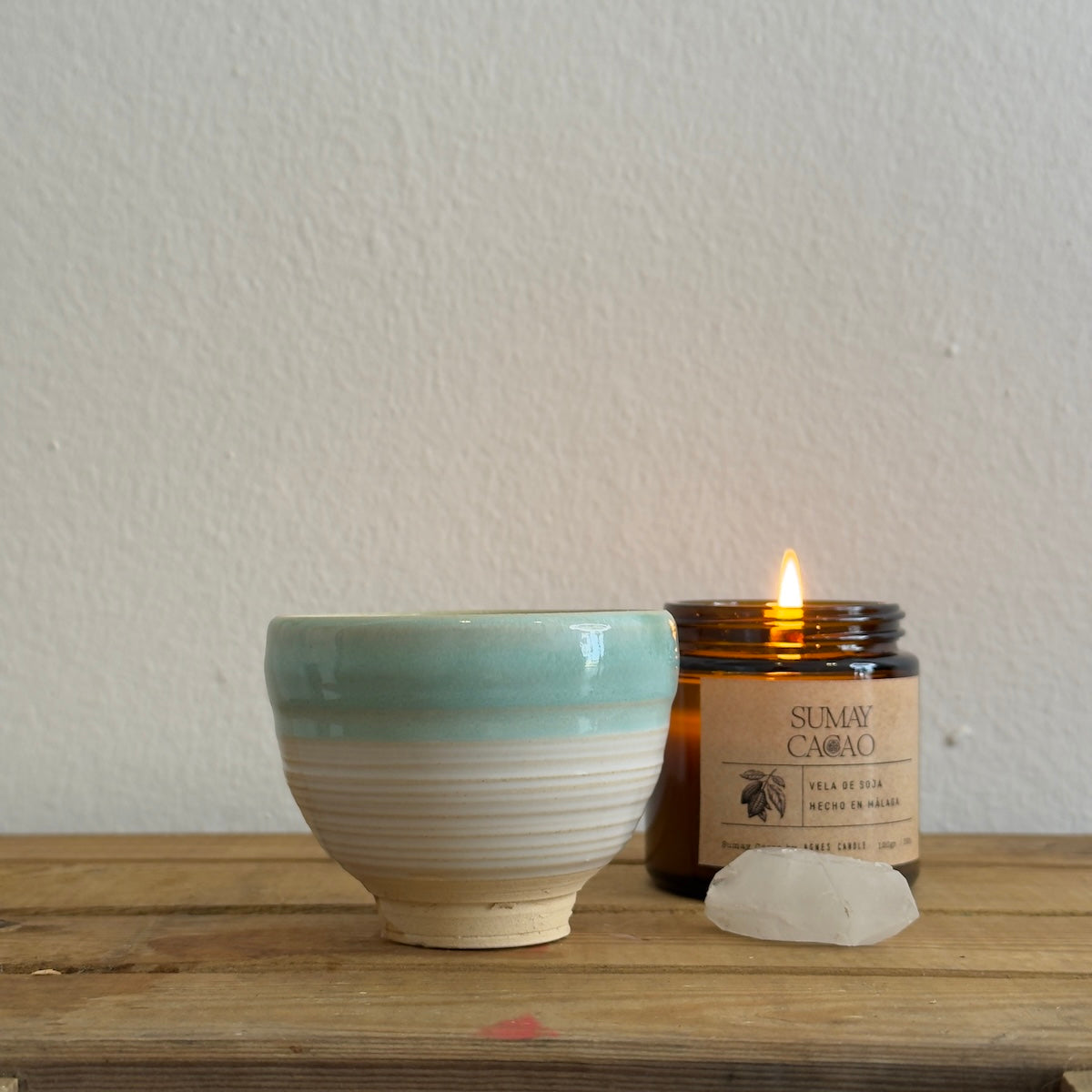 Taza hecha a mano para Sumay Cacao con vela encendida y cuarzo sobre madera y fondo blanco
