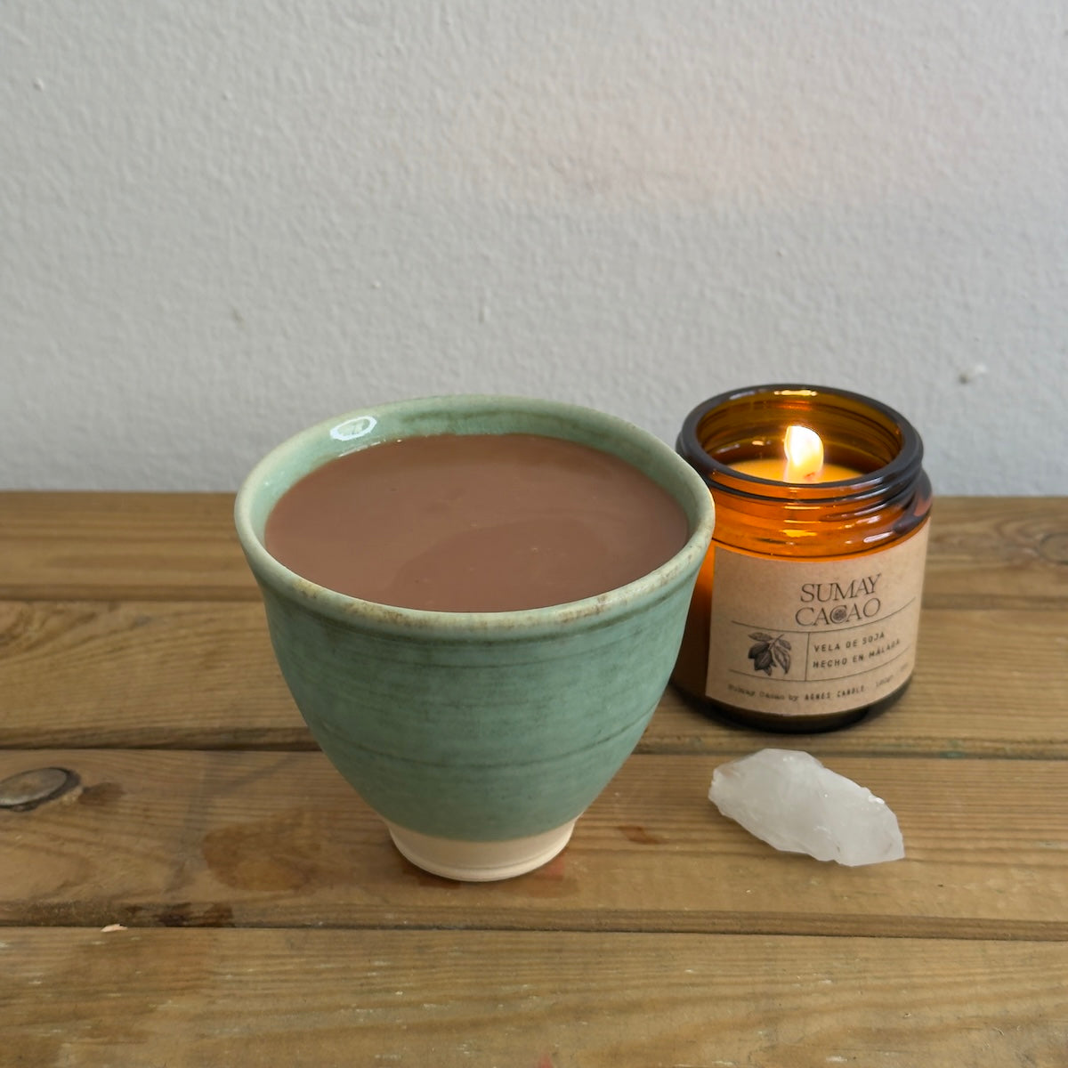 Mesa de madera con vela encendida, cuarzo y taza con cacao ceremonial de Sumay Cacao.