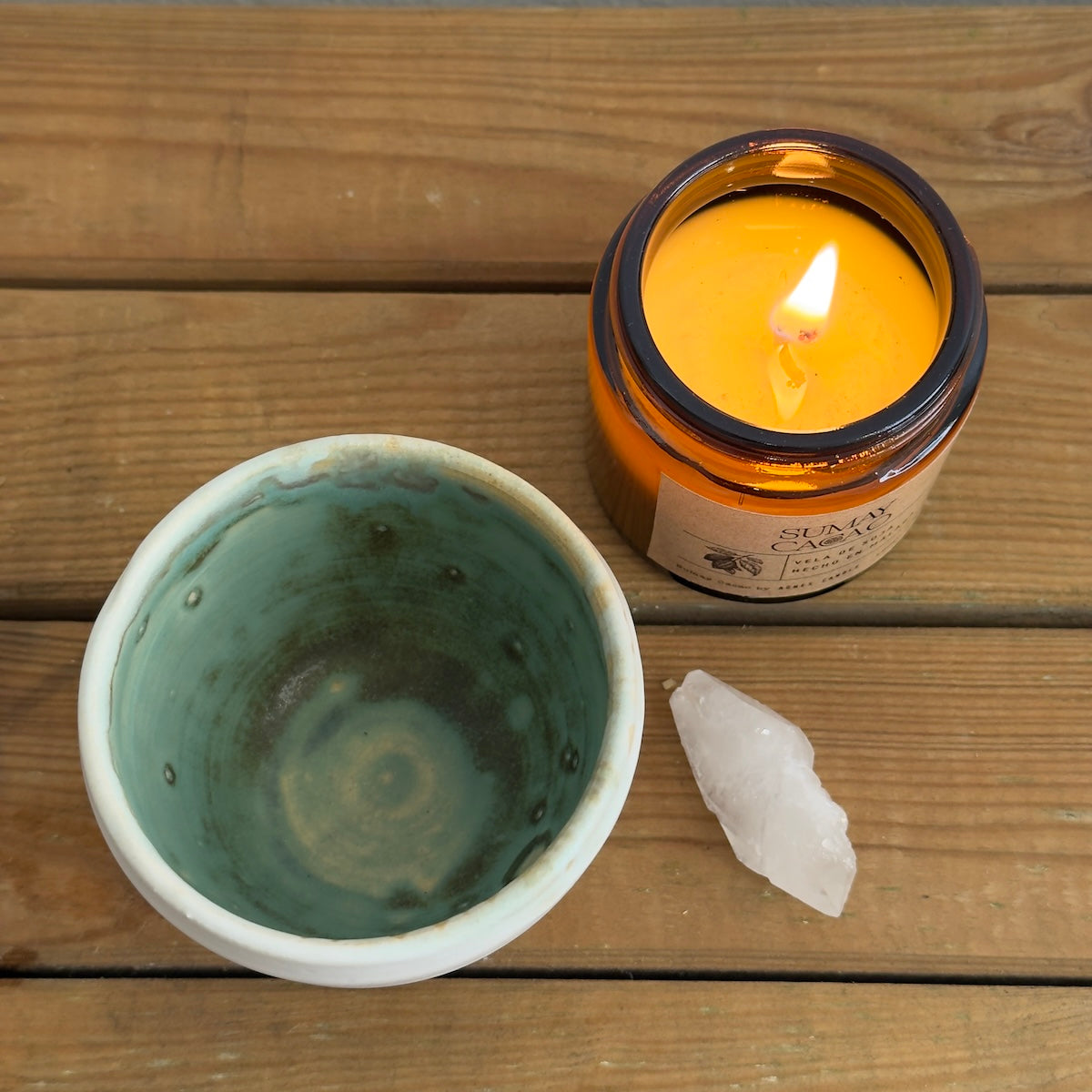 Taza artesanal de cerámica con esmalte verde con cuarzo y vela de soja sobre mesa de madera.