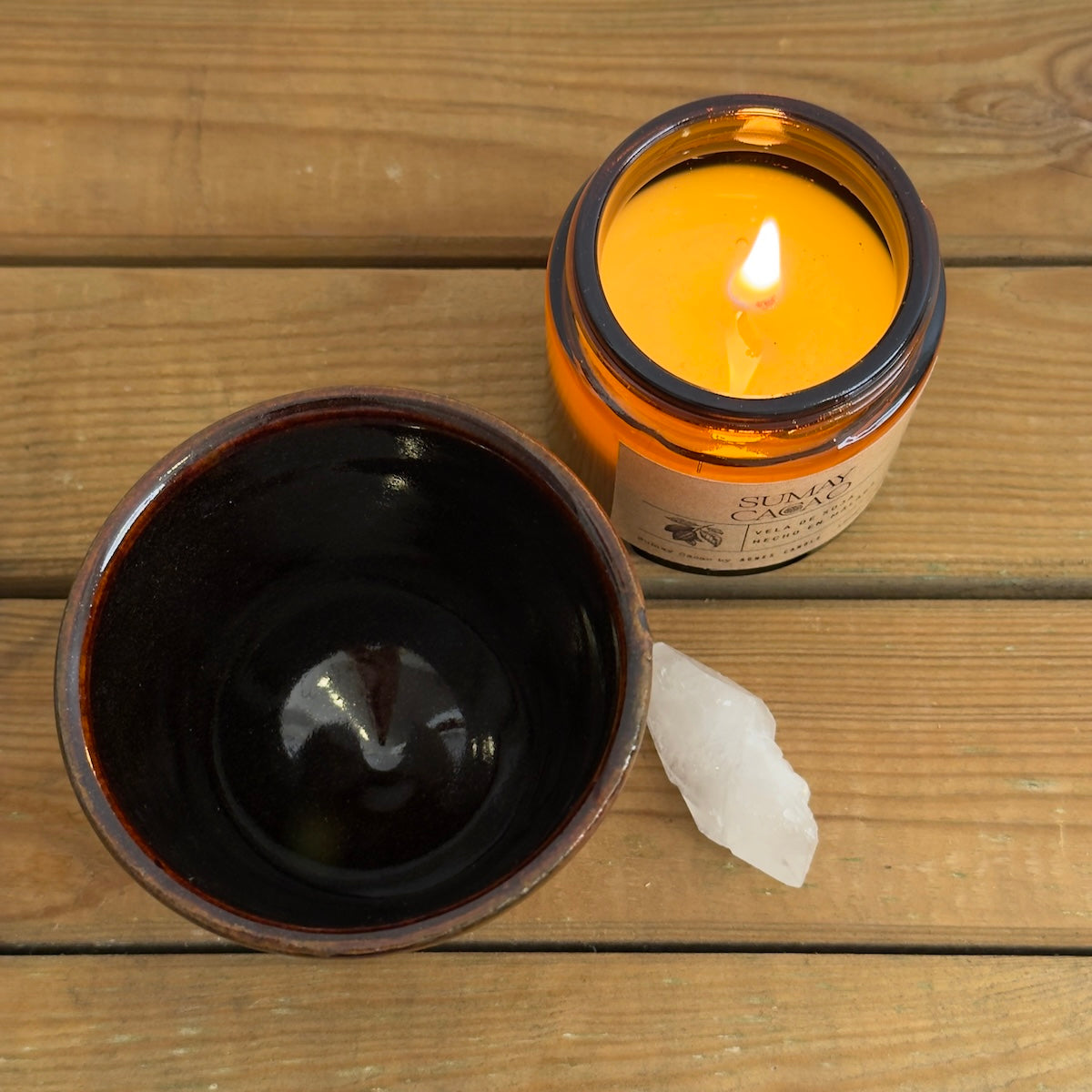 Taza marrón con cuarzo y vela encendida sobre mesa de madera, cerámica artesanal.