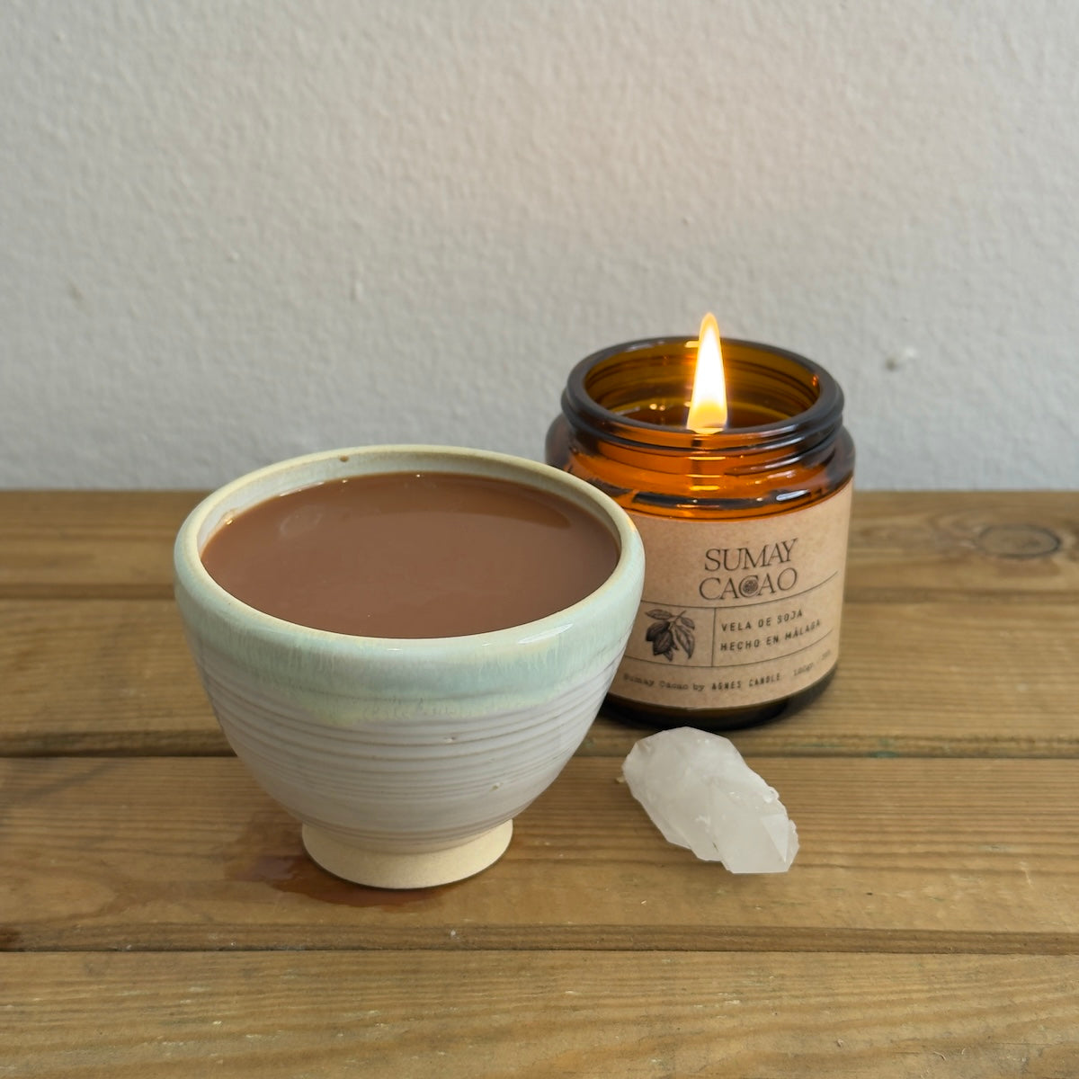 Taza para cacao ceremonial con cuarzo y vela sobre mesa madera y fondo blanco.