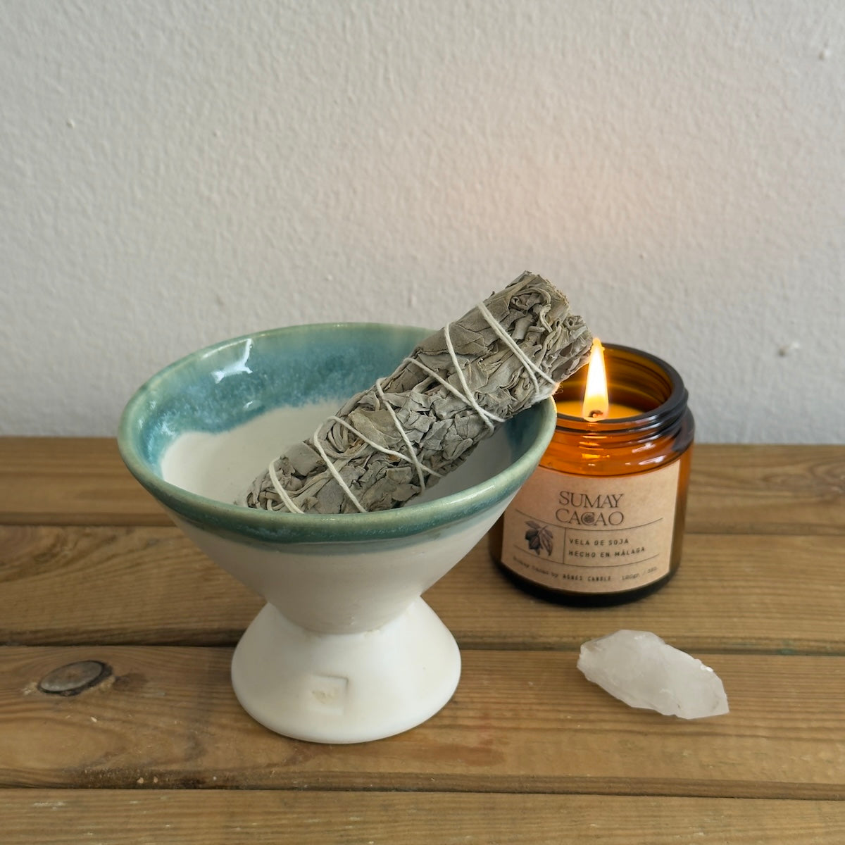 Copalera artesanal con salvia, vela y cuarzo sobre mesa de madera y fondo blanco.