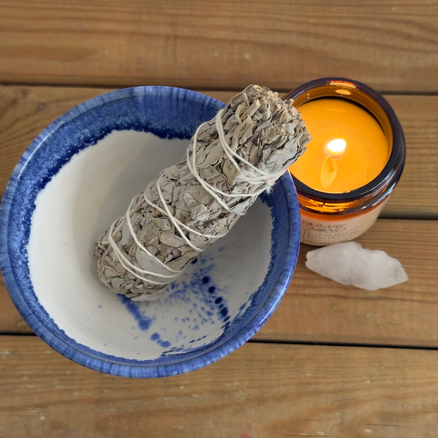 Sahumador artesanal de cerámica con salvia y vela sobre mesa de madera.