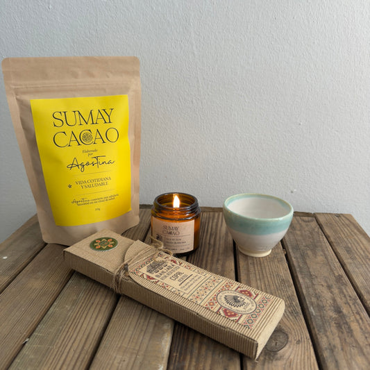 Paquete de cacao premium, copal, taza artesanal, vela de soja, sobre mesa de madera y pared blanca.