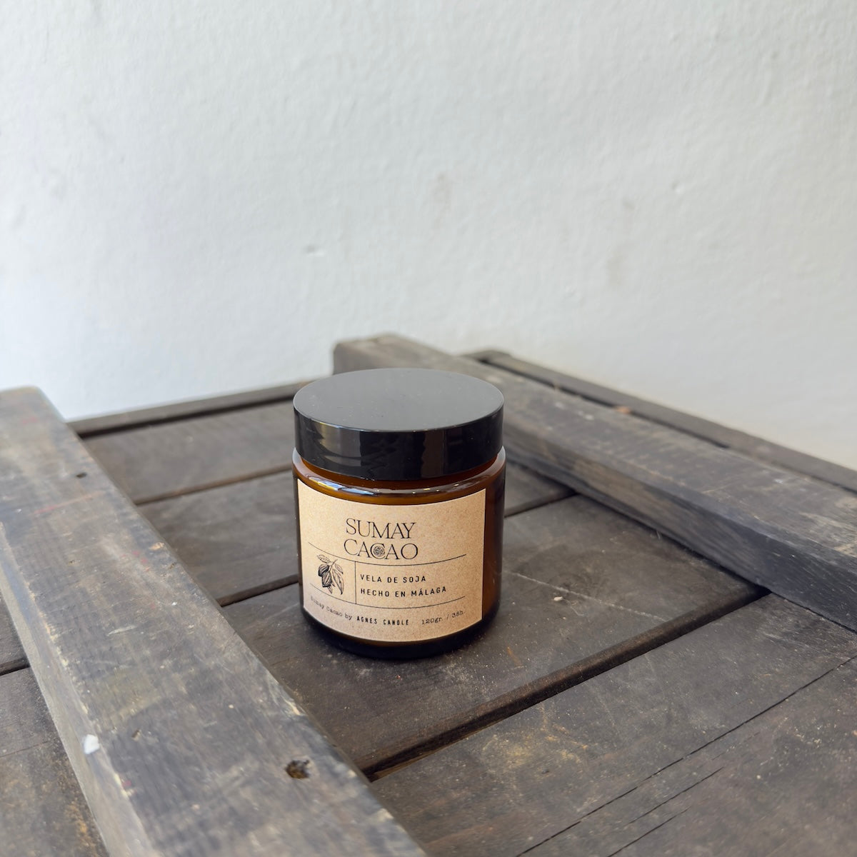 Vela de soja Sumay Cacao, en frasco marrón con tapa, sobre cajón de madera y fondo blanco.