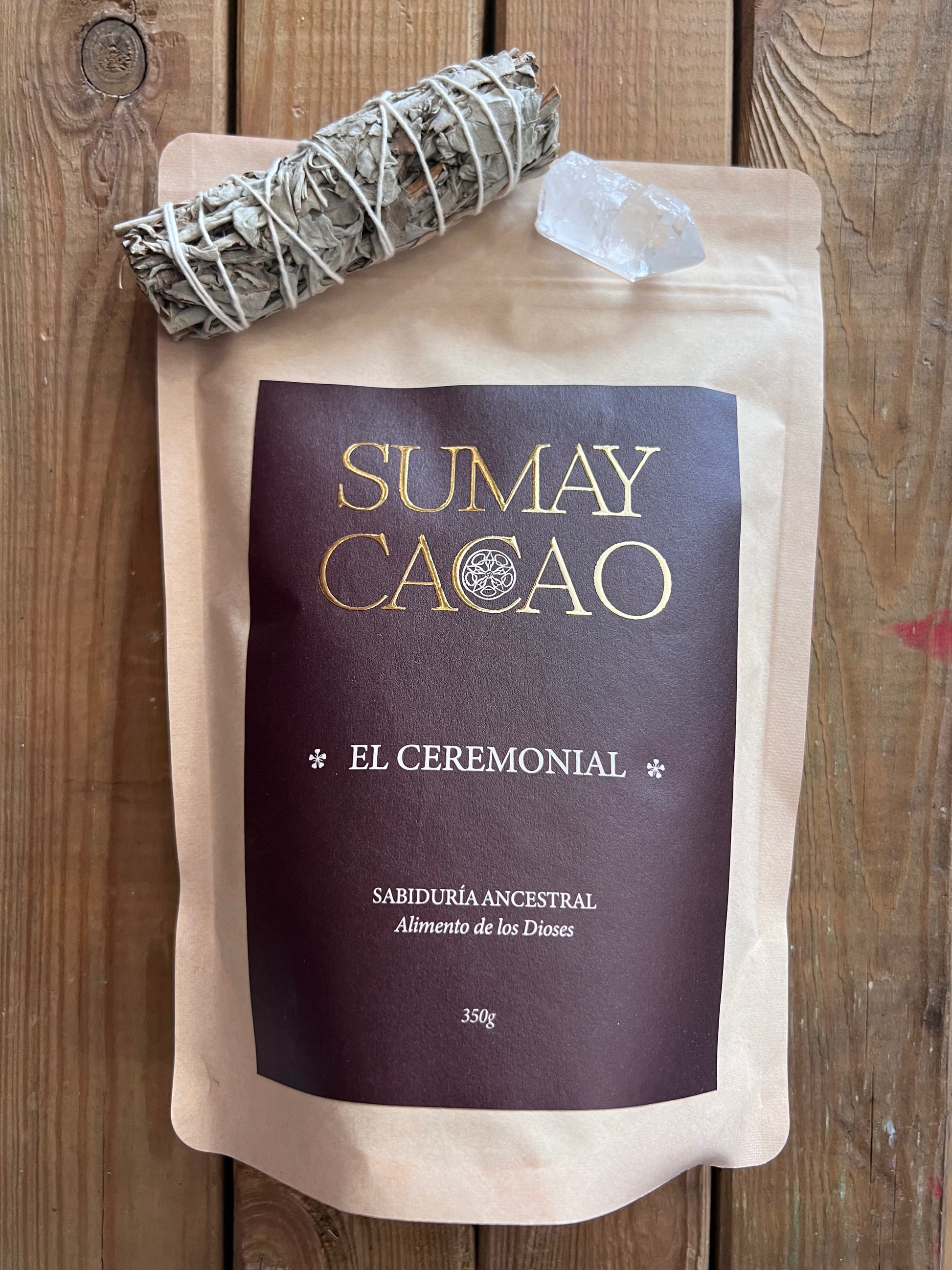 Bolsa de cacao ceremonial Sumay colocada de lado, con salvia y cuarzo encima, sobre fondo madera.