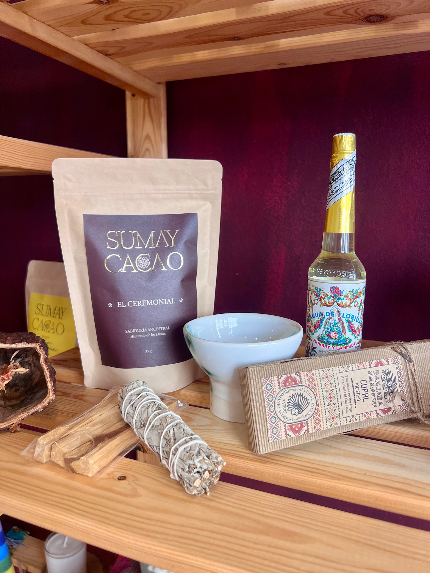Paquete de Cacao ceremonial Sumay con botella agua florida, palo santo, atado de salvia, copalera y copal, sobre estantería de madera