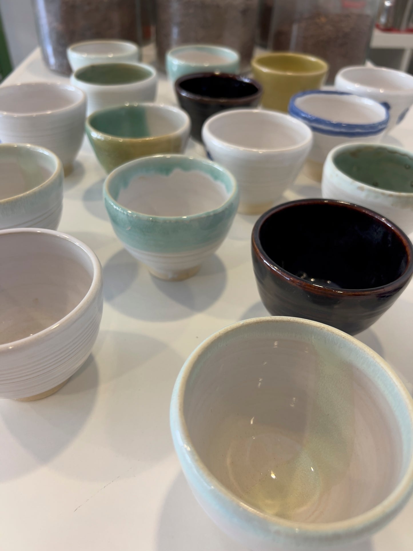 Tazas de cerámica artesanal de diferentes colores sobre mesa blanca