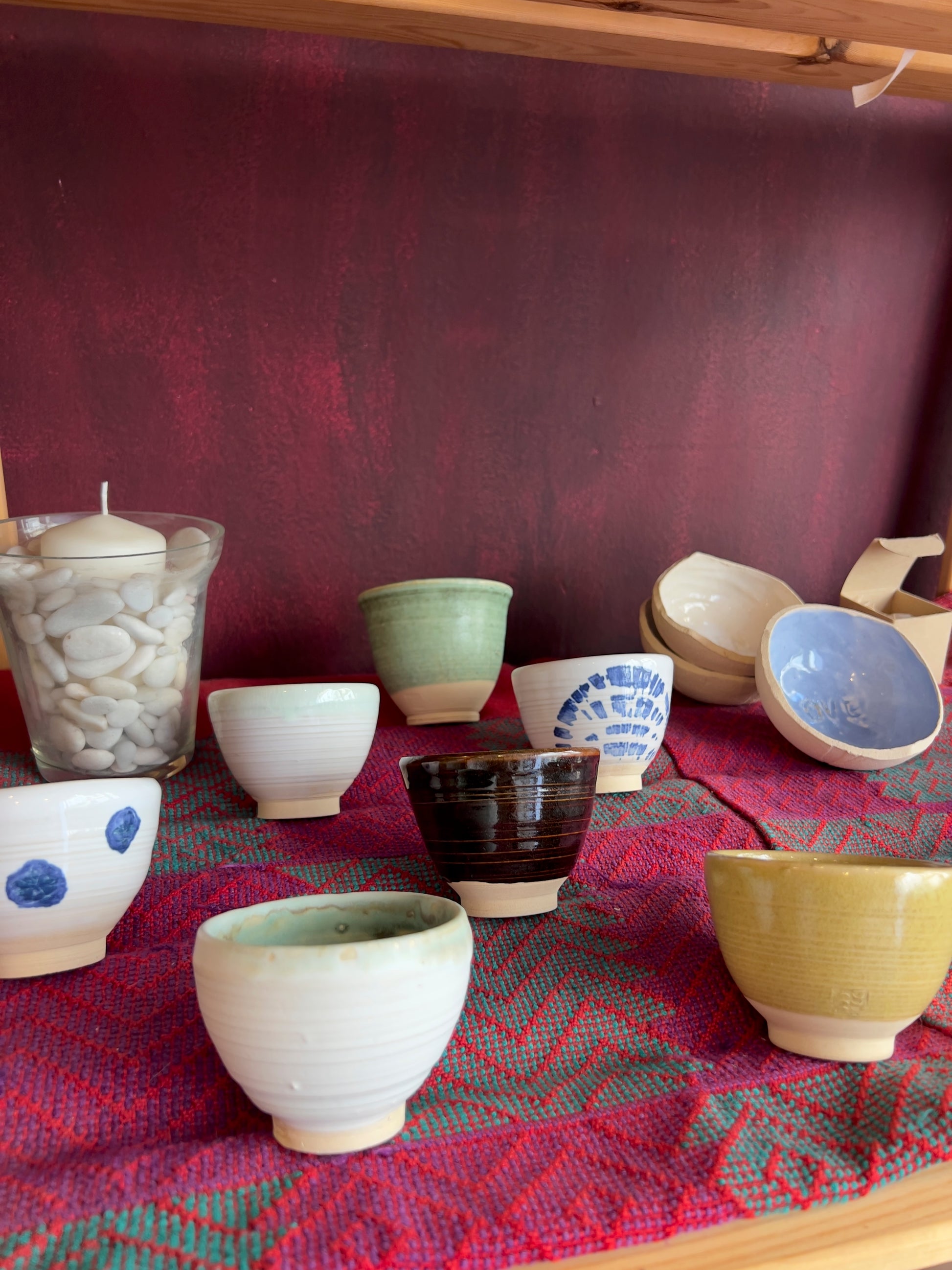 Tazas artesanales de Isa Boyd, diferentes diseños y colores, sobre fondo rojo oscuro.