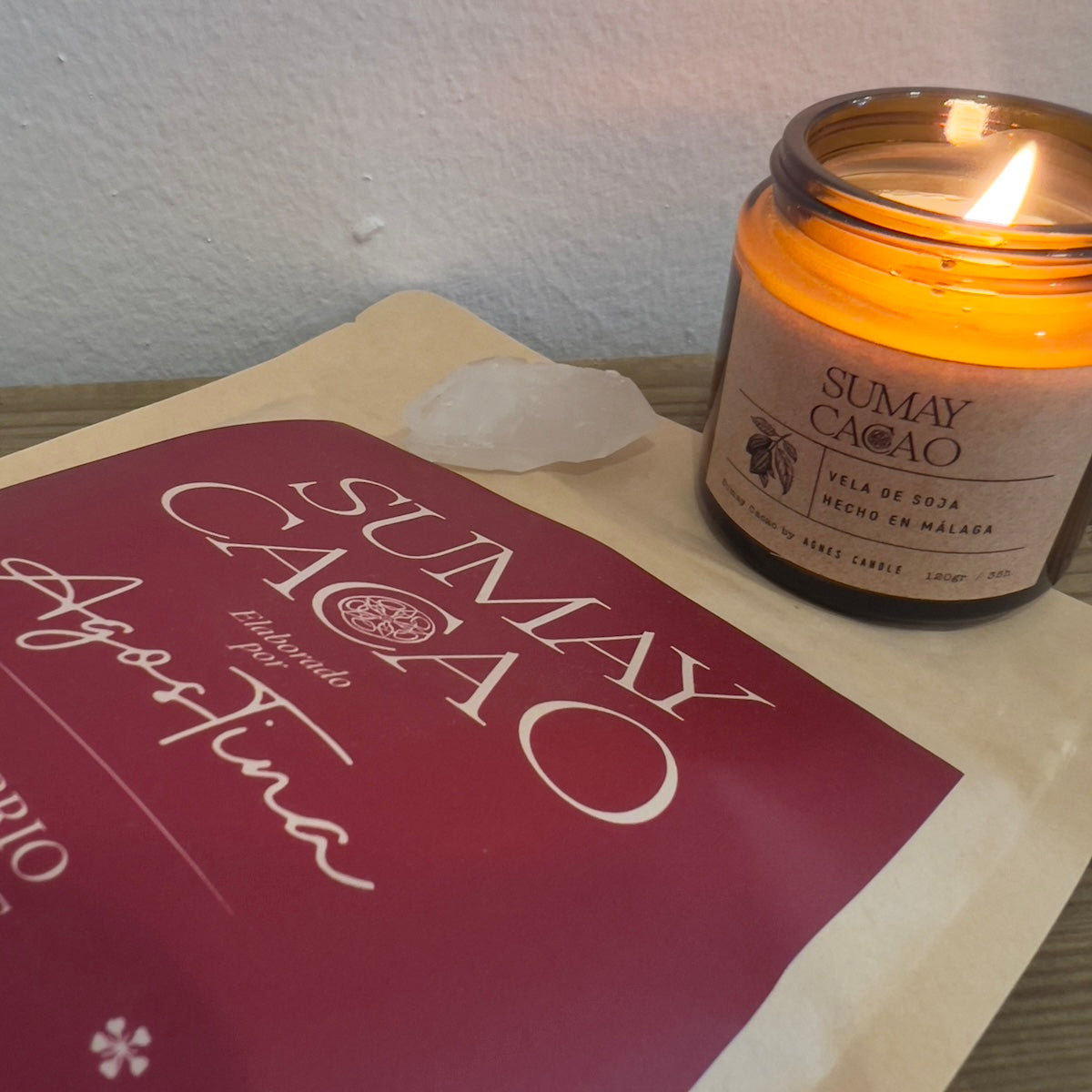 Paquete de cacao Sumay tumbado con cuerzo y vela artesanal encima, fondo blanco.