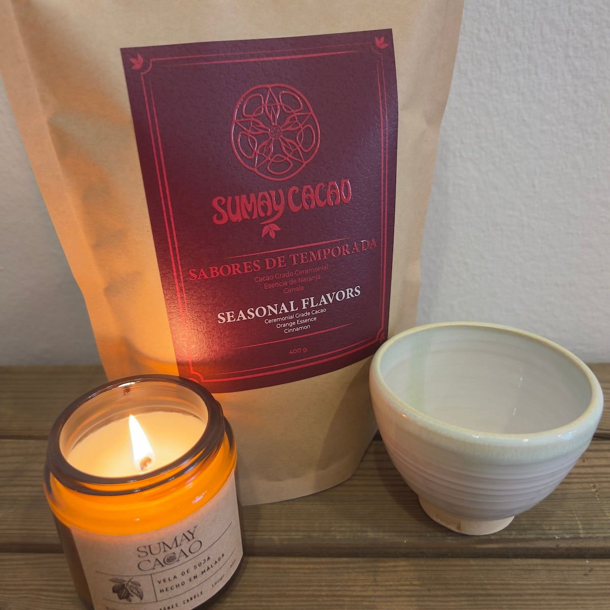 Sobre mesa de madera, taza de Isa Boyd, vela y paquete de cacao ceremonial.