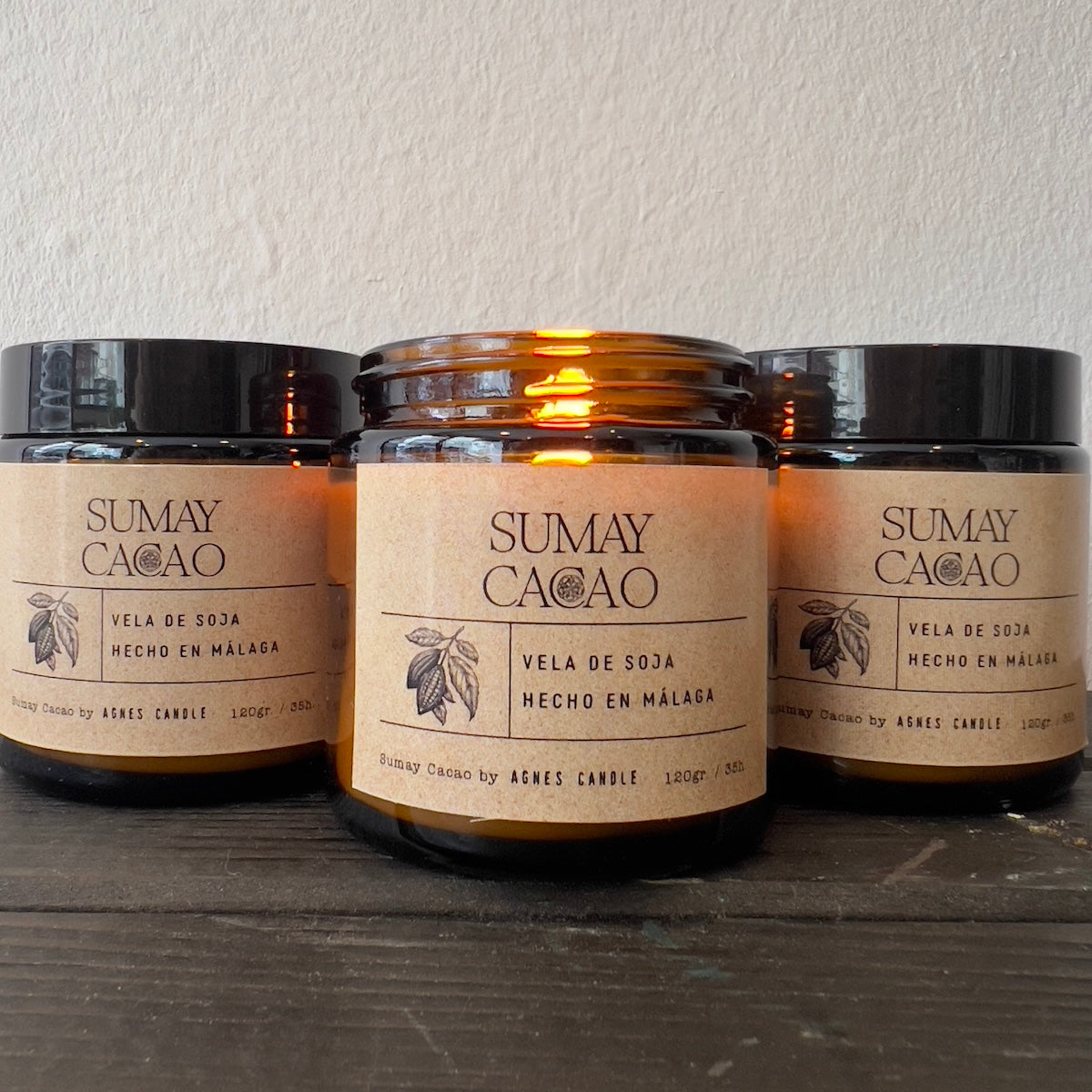 Velas en frascos de cristal marrón sobre mesa de madera con fondo blanco.