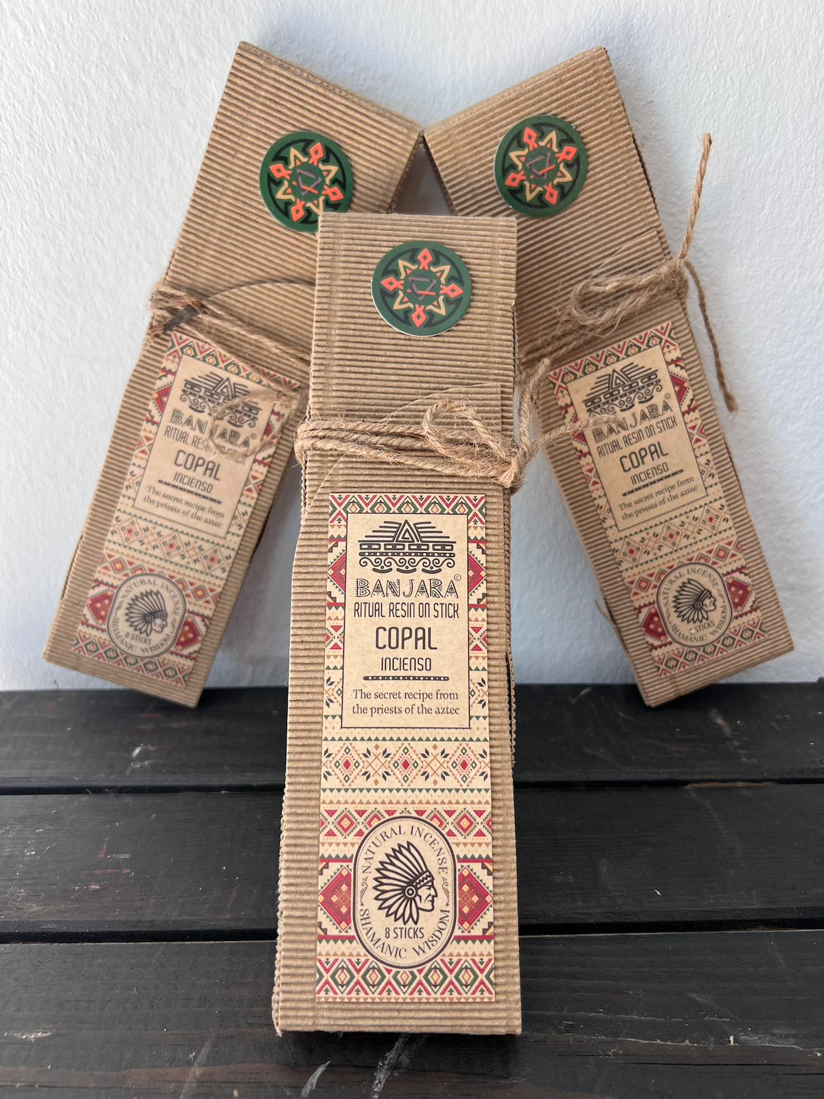 3 paquetes de copal en sticks sobre mesa madera oscura y fondo blanco.