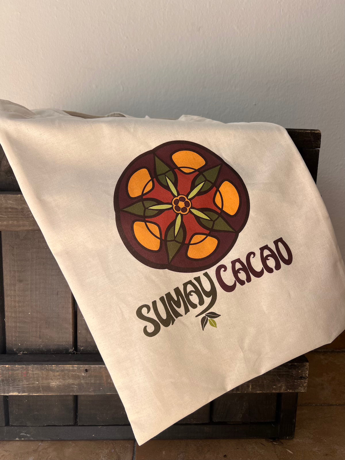 Bolsa de tela con logo de Sumay Cacao sobre cajón de madera.