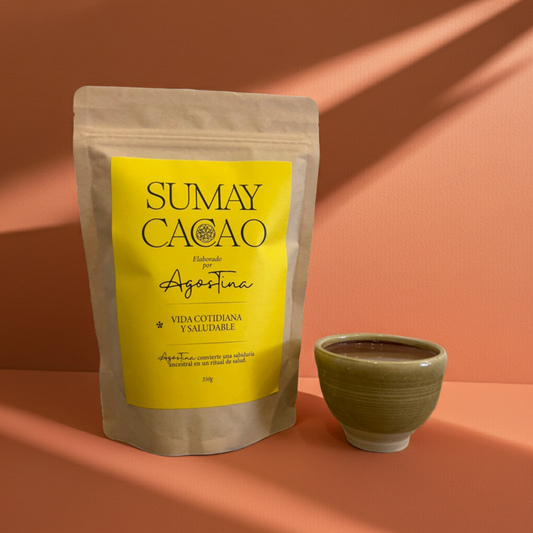 Bolsa de pasta de cacao ceremonial Sumay Cacao Vida Cotidiana 350 g junto a una taza de cacao caliente sobre fondo melocotón, iluminación cálida y sombras naturales.
